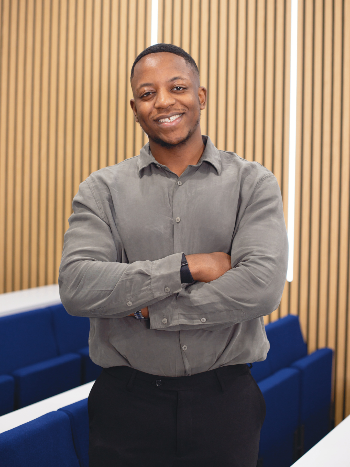 Malone Mukwende standing in a lecture theatre, smiling with arms crossed